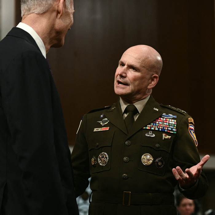 A man in a suit speaking with a man in a military uniform.