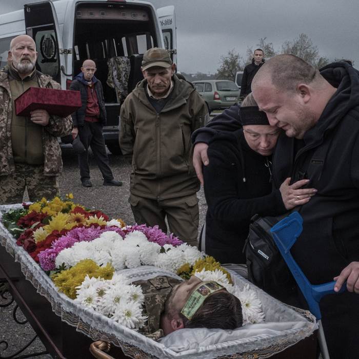 People surround a man in a coffin covered in flowers.