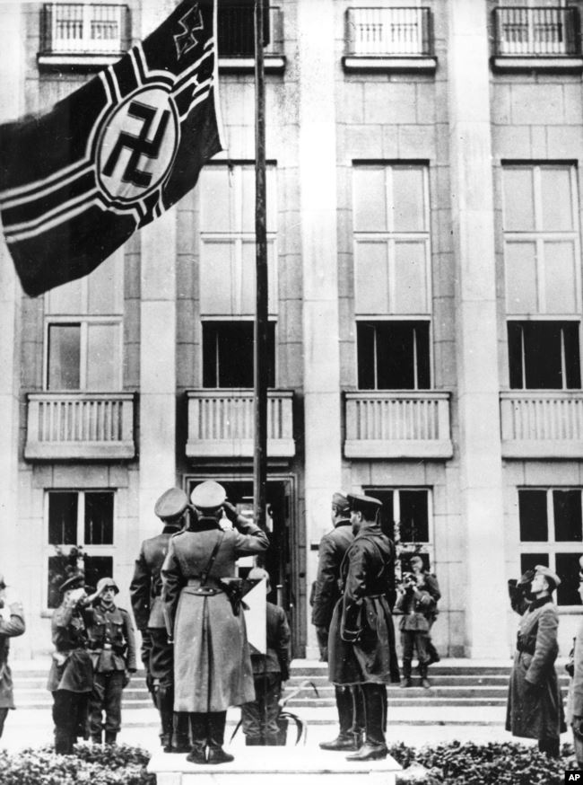 Військовослужбовці нацистської Німеччини і СРСР віддають честь німецькому прапорові зі свастикою під час урочистостей у рамках військового параду з нагоди поділу земель, що належали до того Польщі. Брест-Литовський, 22 вересня 1939 року